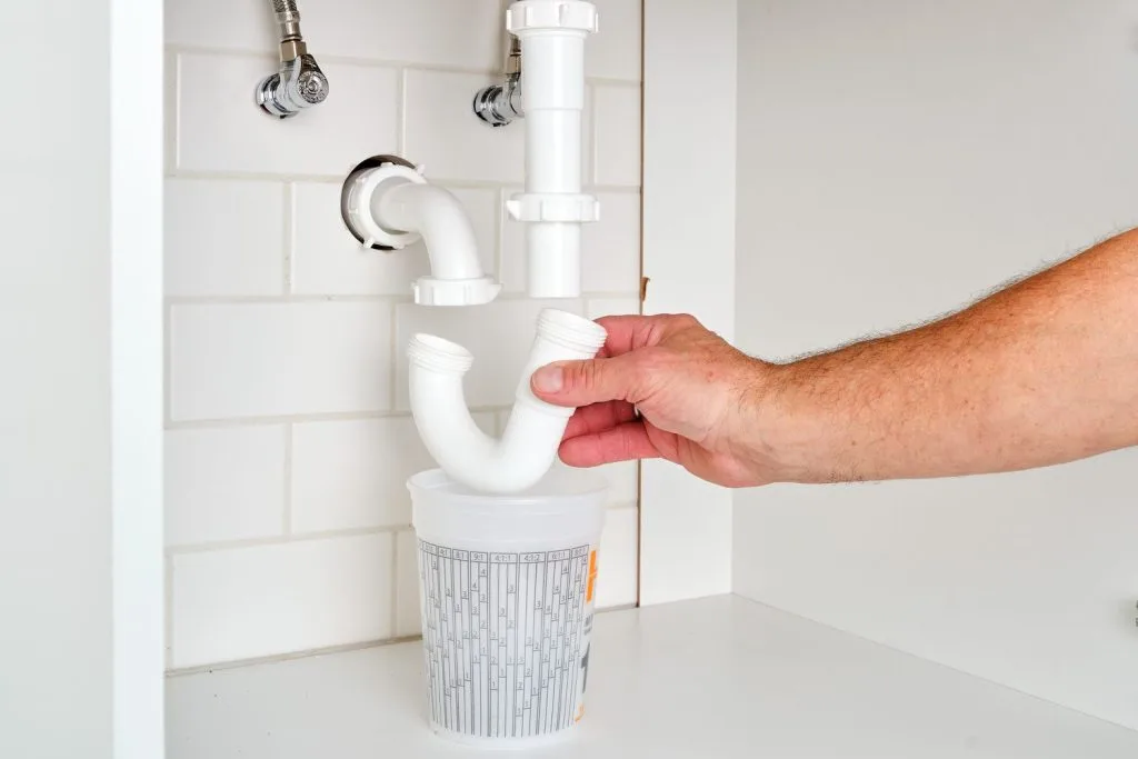 person disconnecting the sink’s U trap (the curved pipe) to clean it