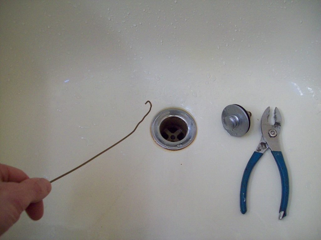 person using a bent wire coat hanger to clear a drain