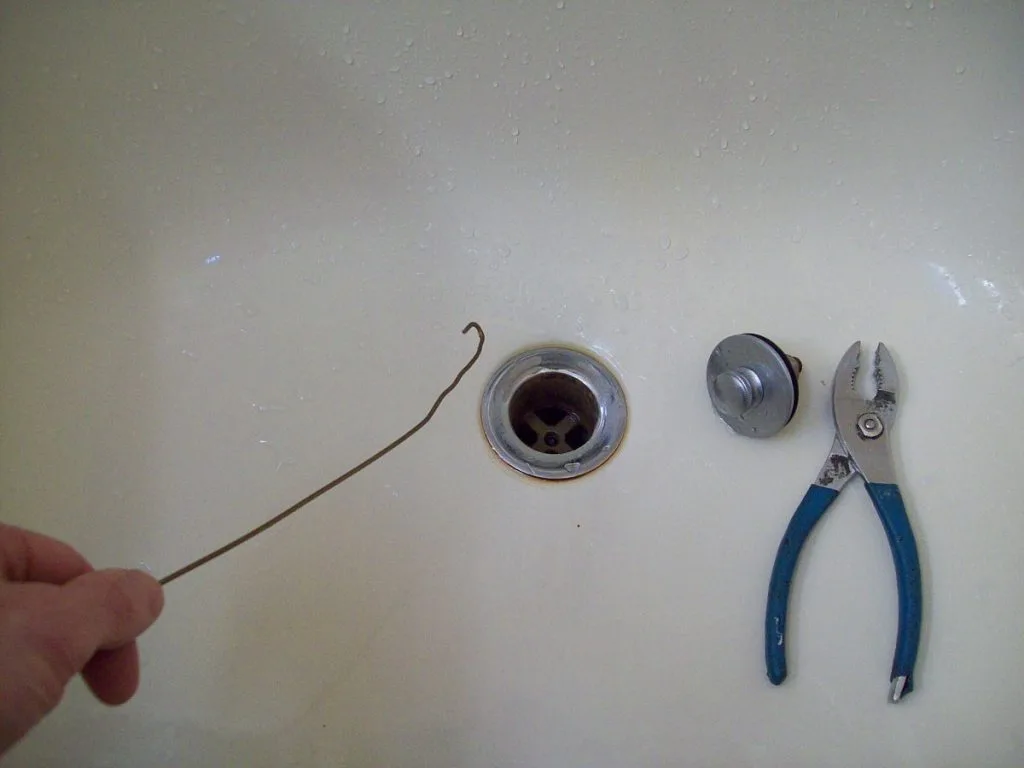 person using a bent wire coat hanger to clear a drain
